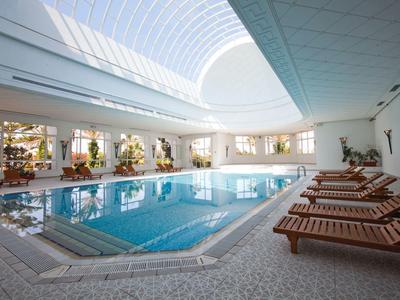 Innenpoolbereich mit Sonnenliegen und großer Glasdecke in einem Hotel.