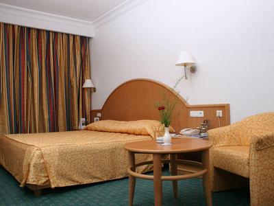 Hotelzimmer mit Doppelbett, Tisch, Stuhl und bunten Vorhängen.