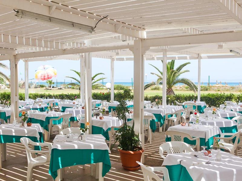 Hell gedeckter Außenbereich eines Restaurants mit Blick auf Palmen und das Meer.