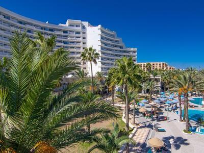 Complexe hôtelier moderne avec piscine et palmiers sous un ciel bleu clair