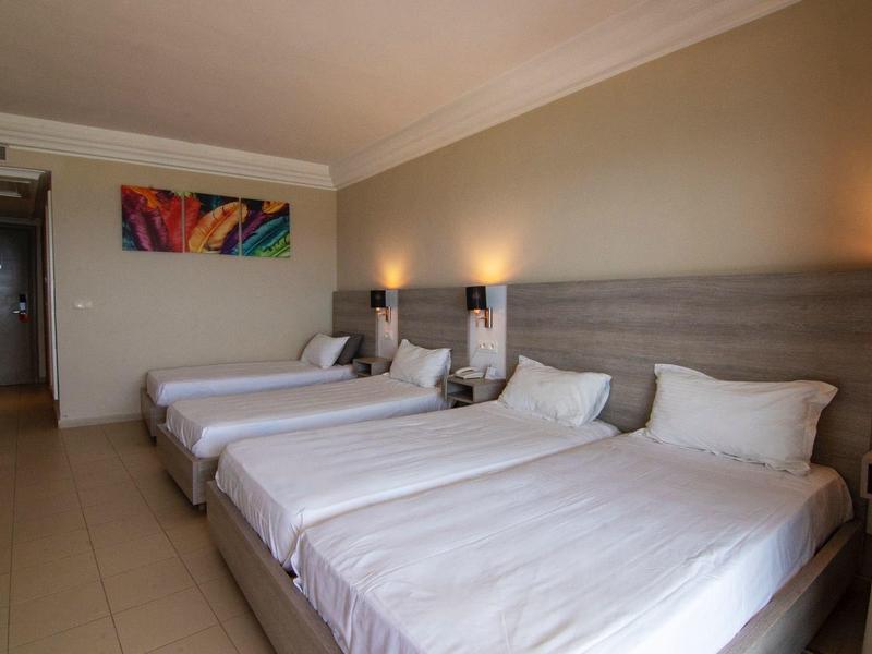 Chambre d'hôtel avec trois grands lits alignés et tableau coloré au mur.