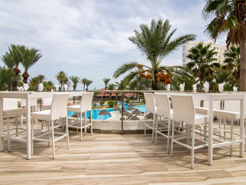 Espace extérieur moderne avec chaises et piscine, entouré de palmiers et ciel bleu.