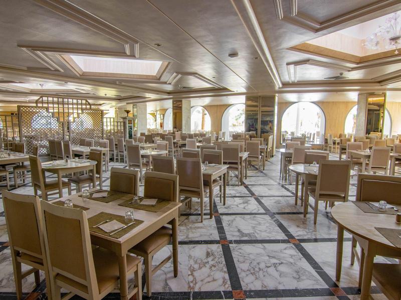 Grande salle à manger élégante avec de nombreuses tables et chaises sous un éclairage chaleureux.