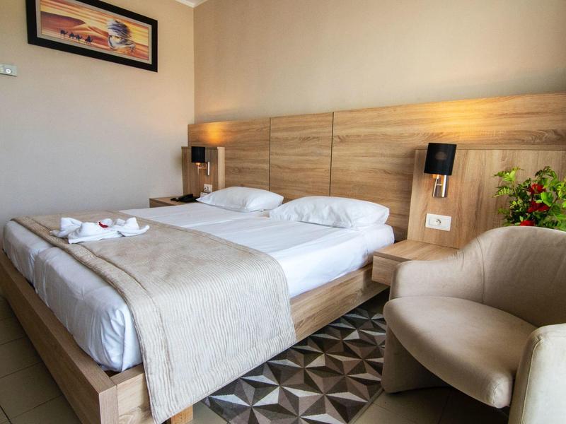 Chambre d'hôtel moderne avec lit double, fauteuil, tapis et plantes.