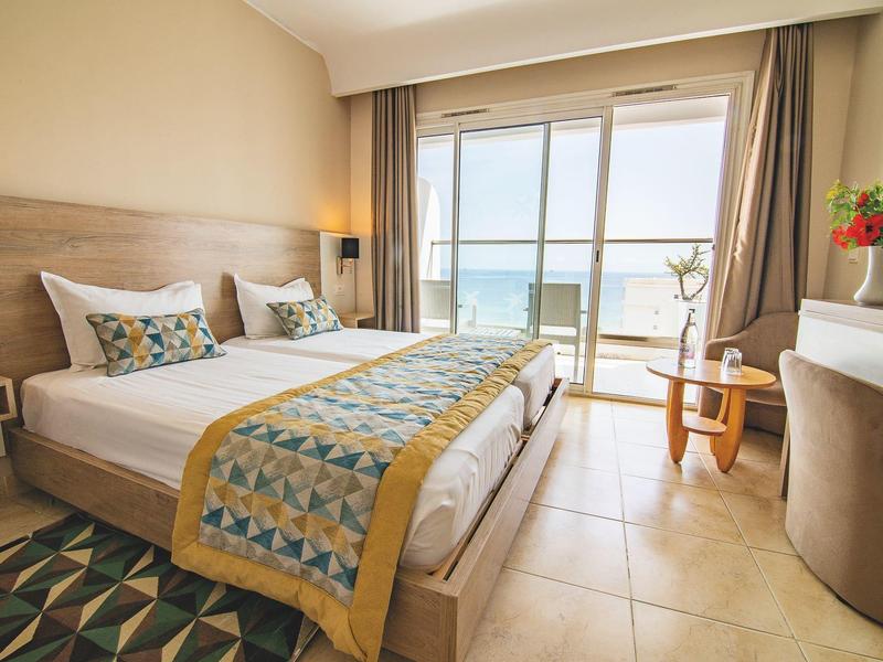 Chambre d'hôtel lumineuse avec lit double, vue sur mer depuis le balcon.