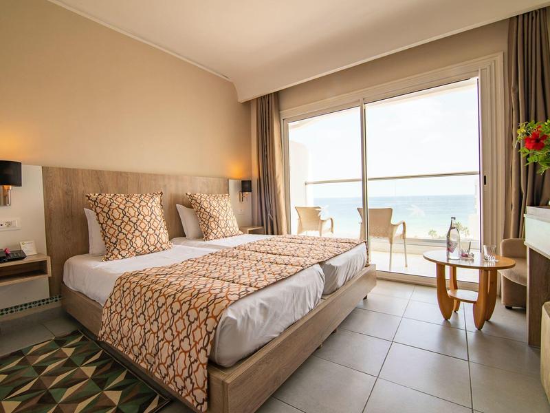 Chambre d'hôtel lumineuse avec lit double et balcon vue mer.