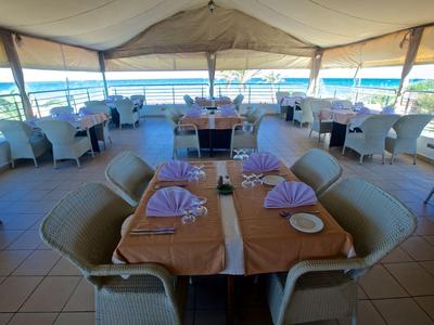 Überdachte Terrasse mit eingedeckten Tischen und Blick auf das Meer.