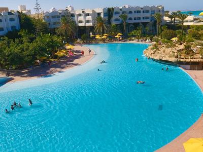 Großer Hotelpool mit klaarem blauem Wasser, umgeben von Liegestühlen und Gebäuden.