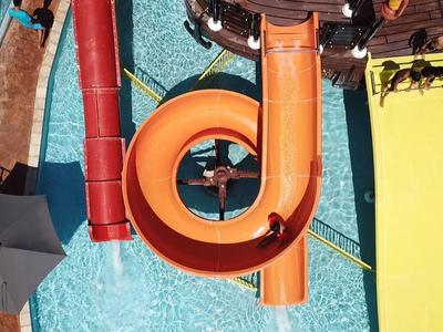Ansicht von oben auf orangefarbene und gelbe Wasserrutschen in einem Poolbereich eines Hotels.