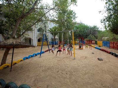 Kinderspielplatz mit mehreren Schaukeln, Sandboden und umgeben von Bäumen und Gebäuden.