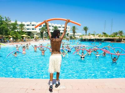 Ein Trainer zeigt Übungen mit Schwimmnudeln, Teilnehmer machen Wassergymnastik im Außenpool.