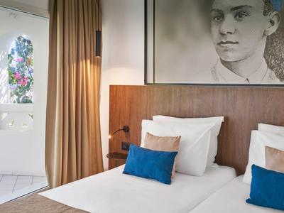 Modernes Zimmer mit zwei Einzelbetten, weißen Kissen, blauen Zierkissen, Holzkopfteil und großem Bild.