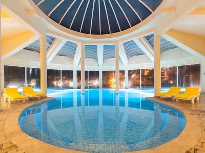 Rundes Hallenbad mit Glaskuppel und gelben Liegestühlen in einem Hotel.
