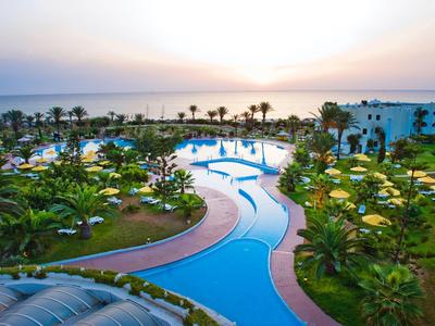 Großer Außenpool mit Palmen und Sonnenschirmen in einem tropischen Hotelresort bei Sonnenuntergang.