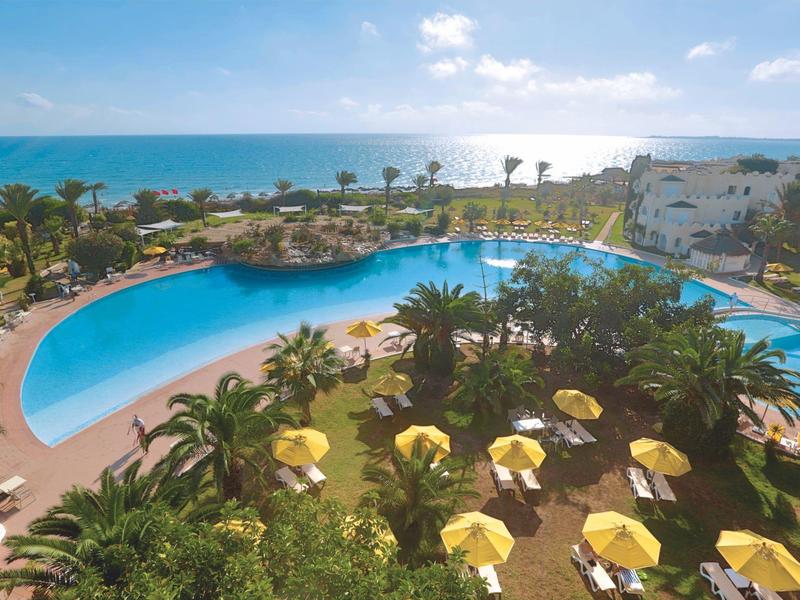 Großer Hotelpool mit Sonnenschirmen und Meerblick am Nachmittag.