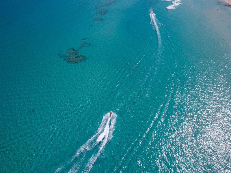 Blick auf einen türkisfarbenen Ozean mit einem Motorboot, das eine weiße Wasserlinie zieht.