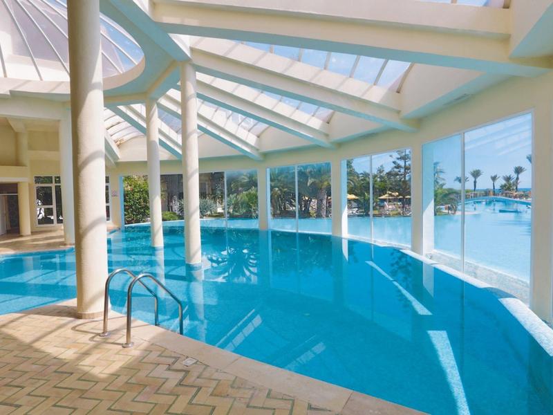 Innenpool mit großen Fenstern und Palmenblick im Außenbereich.