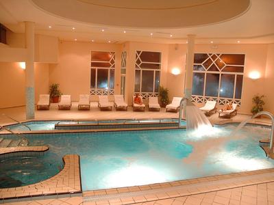 Indoor pool with jacuzzi and waterfall in a modern hotel interior.