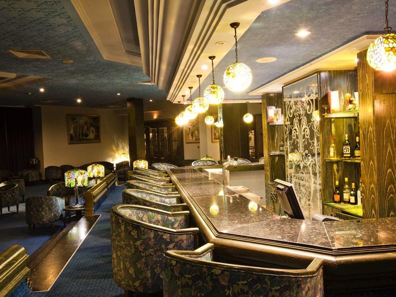 Elegant hotel bar with illuminated counter, bar stools, and subdued lighting.