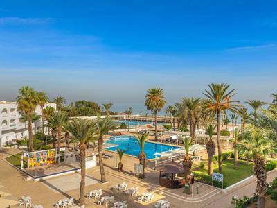 Hotelanlage mit Pool, Palmen und blassblauem Himmel an einem sonnigen Tag.
