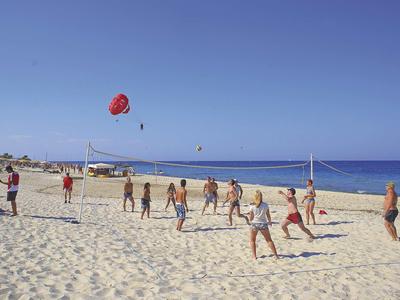 Mehrere Personen spielen Beachvolleyball auf einem weißen Sandstrand unter klarem blauem Himmel.
