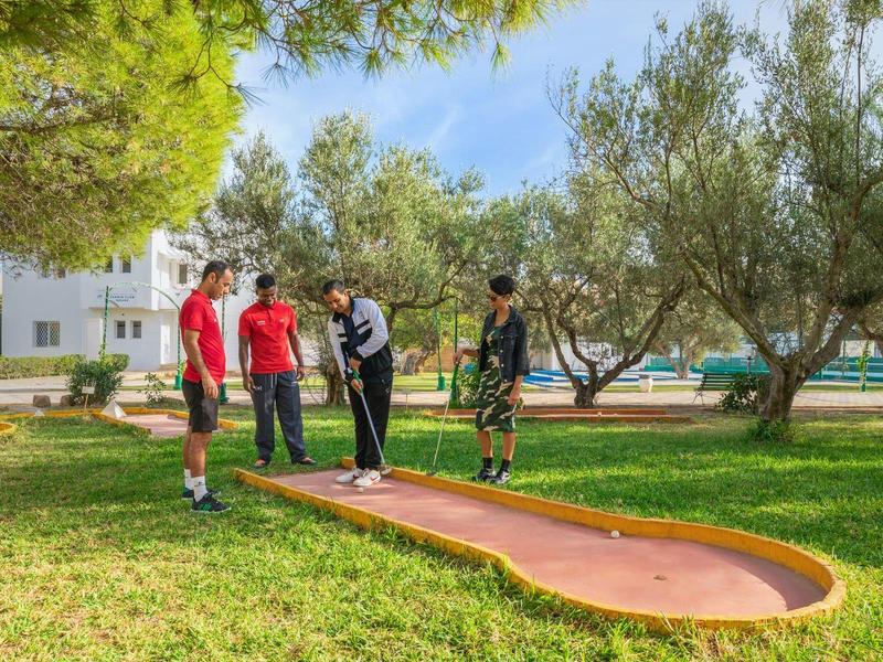 Quatre personnes jouent au mini-golf sur un parcours extérieur par temps ensoleillé.
