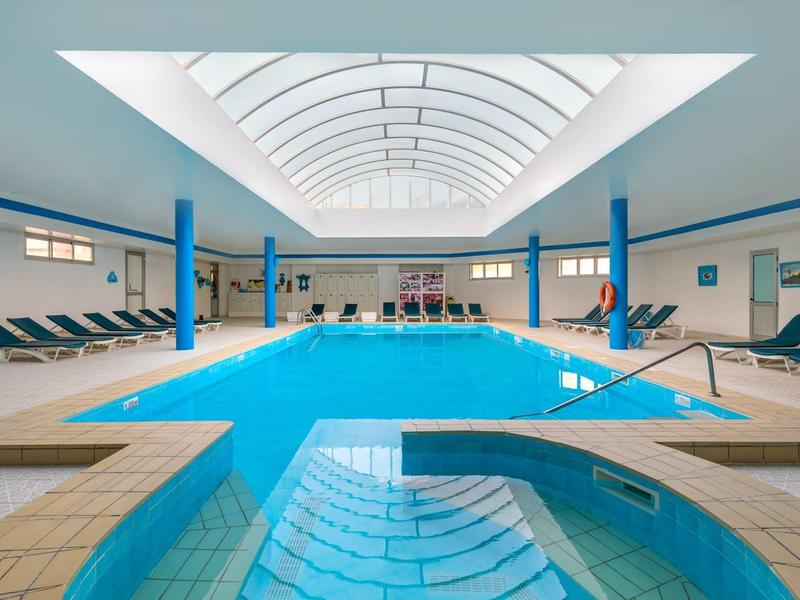 Piscine intérieure lumineuse avec chaises longues et fontaine dans un hôtel.