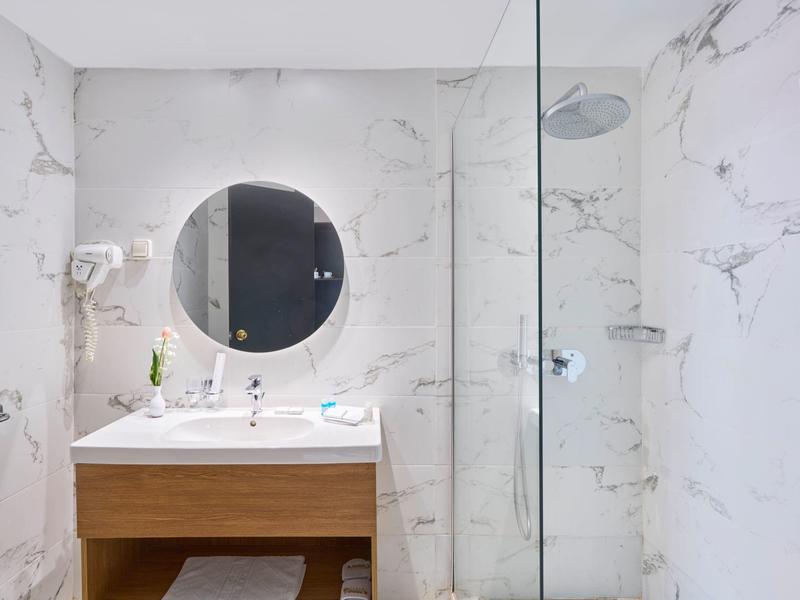 Bright bathroom with round mirror, wooden vanity, and glass shower enclosure.