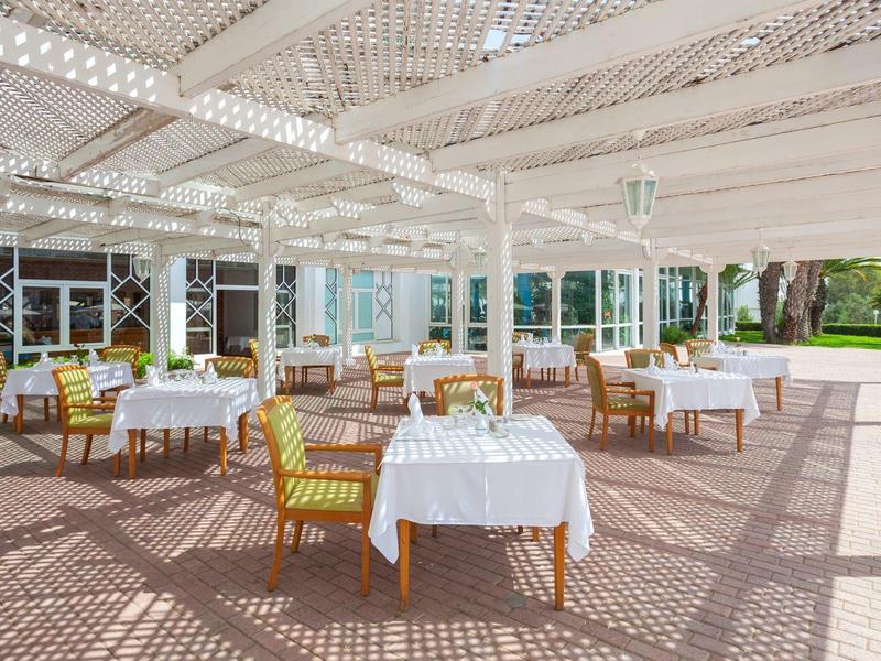 Covered hotel terrace with tables and chairs set for outdoor dining.