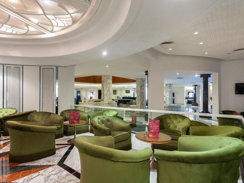 Elegant hotel lounge with green armchairs, round ceiling light, and stylish interior.