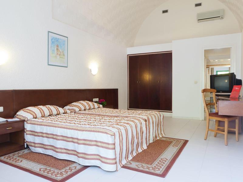 Camera d'hotel semplice con letto matrimoniale, mobili in legno e aria condizionata.