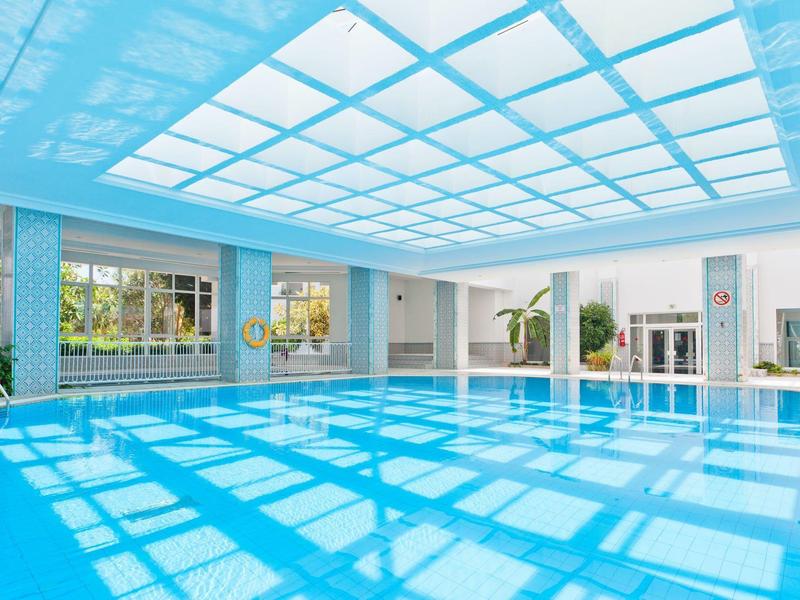 Una grande piscina coperta con acqua azzurra e un soffitto di vetro che fa entrare la luce del giorno.