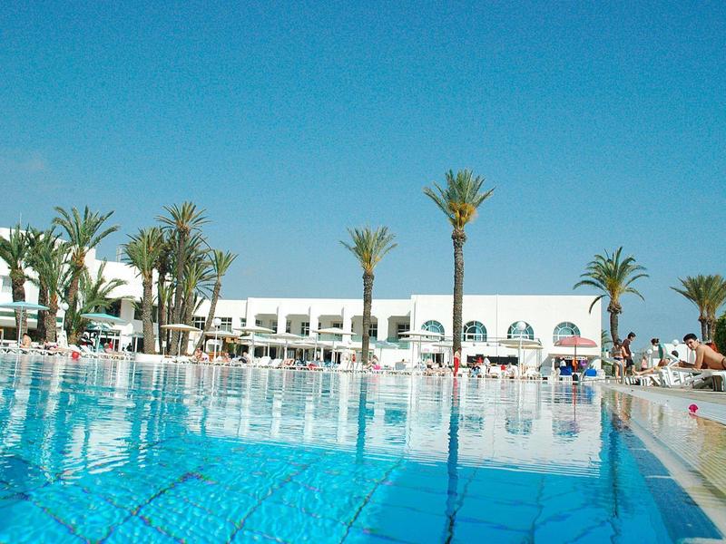 Grande piscina con acqua turchese davanti a un edificio dell'hotel bianco e palme