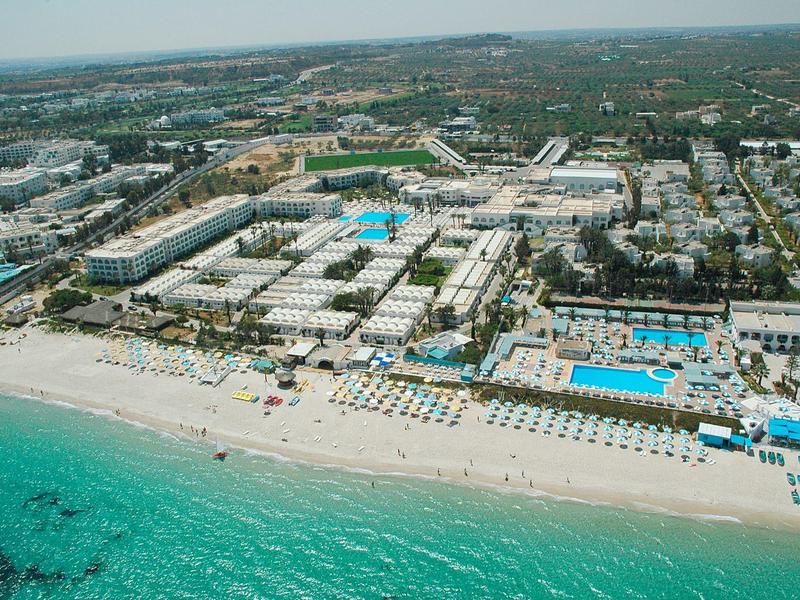 Veduta aerea di un grande resort con più piscine accanto a una spiaggia turchese.