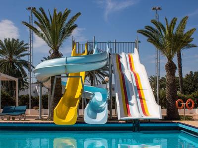 Kolorowe zjeżdżalnie wodne przy basenie z palmami w tle pod niebieskim niebem.