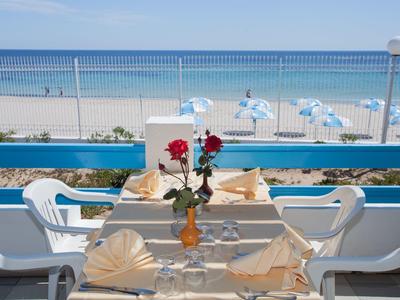 Table with rose and folded napkins on terrace overlooking beach and sea.