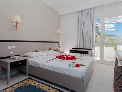Bright hotel room with double bed, nightstands, balcony, and sea view.
