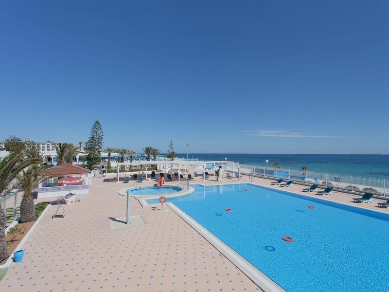 Large outdoor pool with sun loungers and sea view under clear sky.