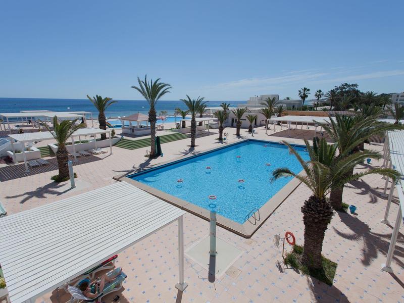 Modern outdoor pool with palm trees and sea view under clear sky at a hotel resort
