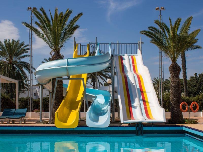 Water park with colorful water slides and palm trees next to a pool under a blue sky.