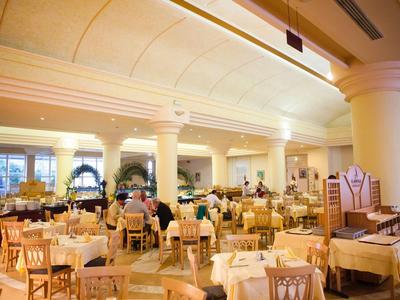 Ampia sala da pranzo ben illuminata con molti tavoli e ospiti.