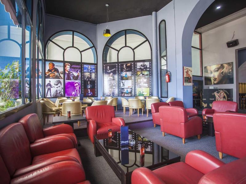 Area lounge accogliente dell'hotel con poltrone rosse davanti a grandi finestre ad arco.