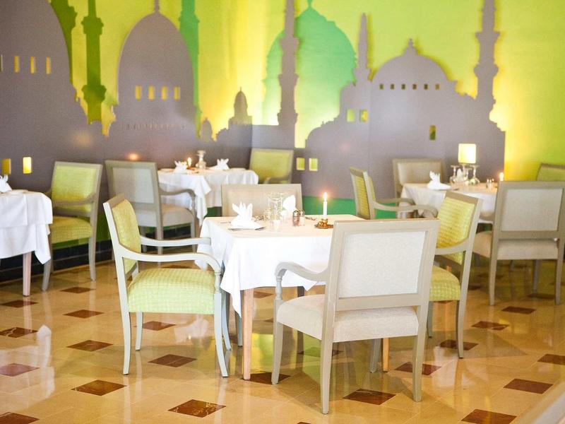 Ristorante luminoso con tavoli e sedie bianchi davanti a una parete con motivo orientale.