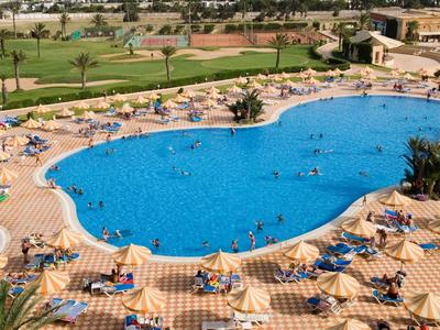 Gran área de piscina con tumbonas y sombrillas en un resort hotelero con clima soleado.