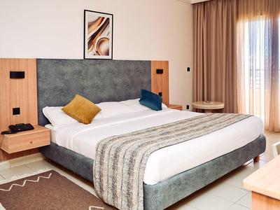 Habitación de hotel moderna con cama grande, cojines decorativos y cortinas en la ventana.