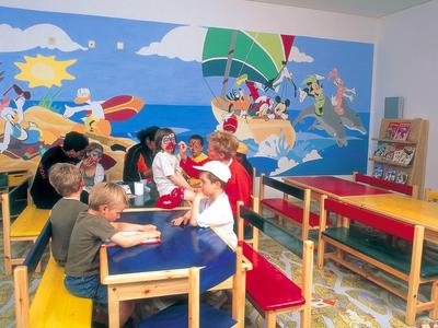 Niños sentados en mesas coloridas en una sala con una gran pintura mural del mar.