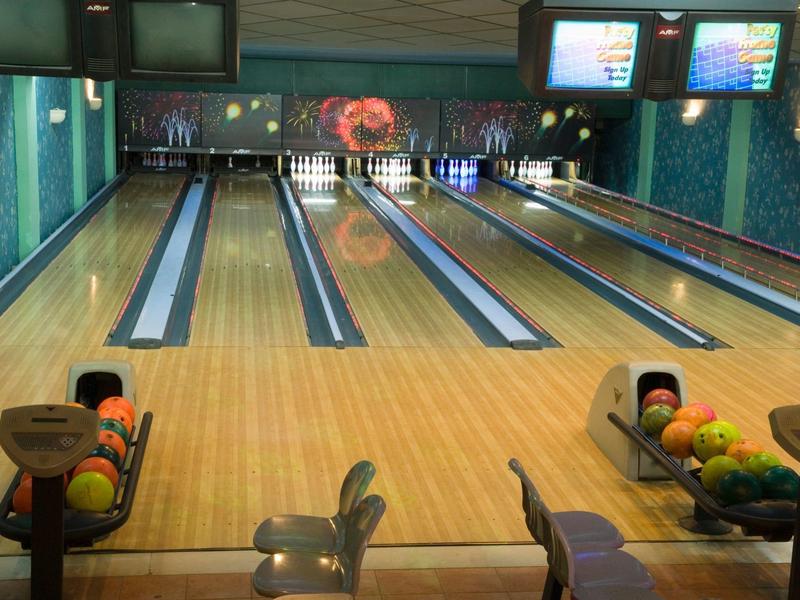 Pista de bolos en un centro de ocio con bolas de colores y pantallas electrónicas.