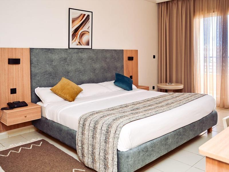 Habitación de hotel moderna con cama grande, cojines decorativos y cortinas en la ventana.