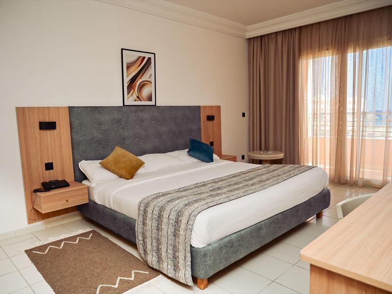 Habitación de hotel cómoda con cama grande, mesitas de noche y cortinas de piso a techo en la ventana.