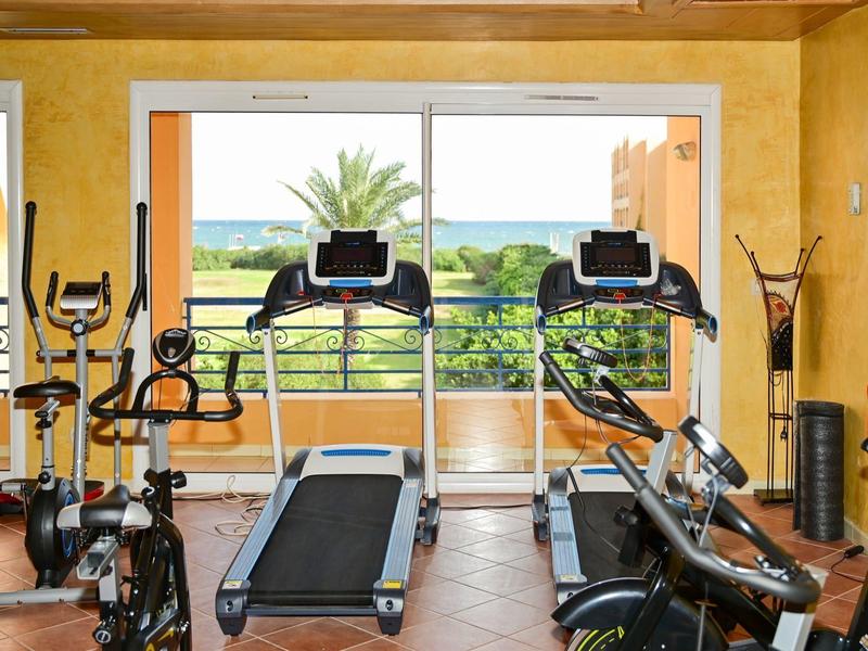 Gimnasio luminoso del hotel con cintas de correr, bicicletas y vista de palmeras y mar.